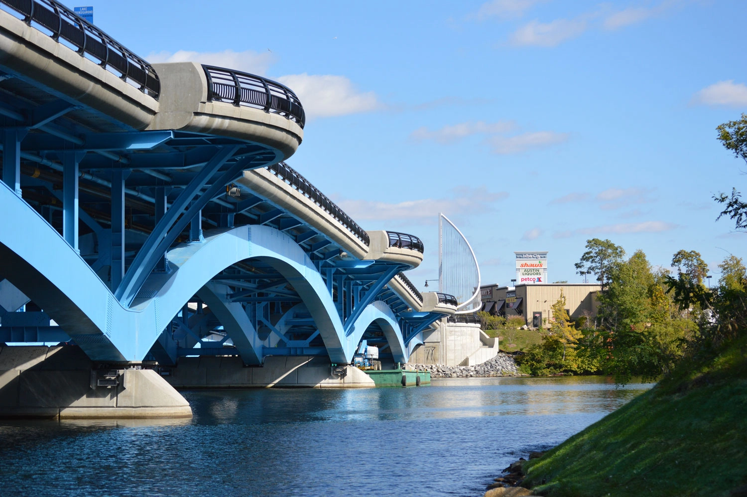 The construction of the Kenneth F. Burns Memorial Bridge was a complex and high-profile project that replaced a structurally deficient, 7-span concrete arch bridge built in 1916 with 2 new bridges over Lake Quinsigamond, between Worcester and Shrewsbury, MA. The new bridges are 870’ long, 5-span open spandrel steel deck arches founded on 36” diameter pipe piles up to 290’ deep. The project also included reconstructed portions of Lake Avenue and Route 9 and contains many architectural features.